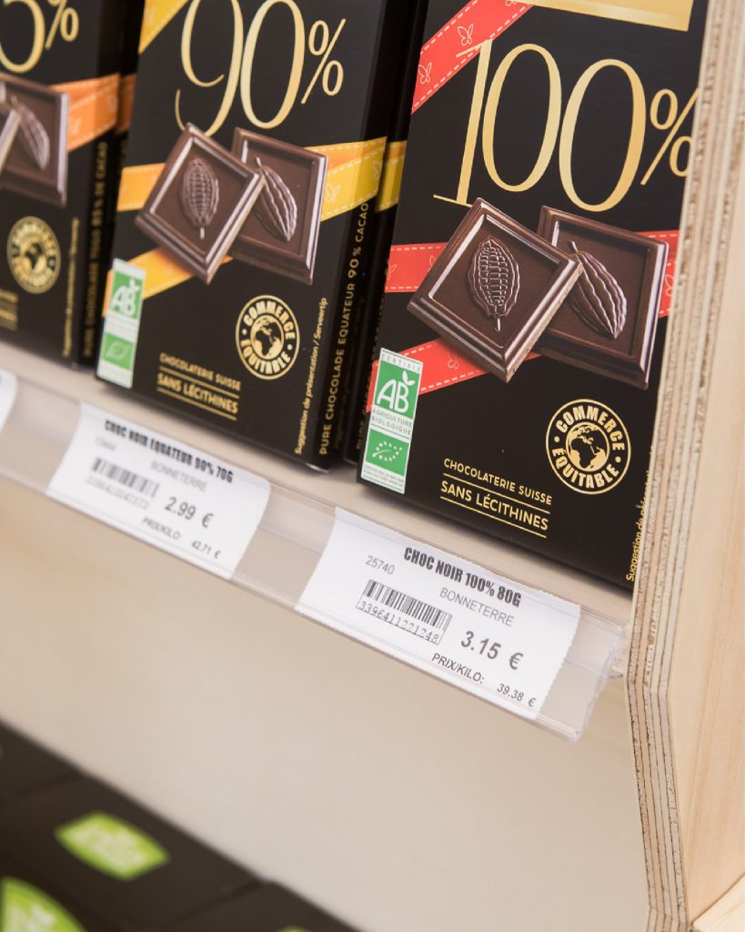 Tablettes de chocolat noir disposées sur un présentoir en bois avec porte-étiquettes transparents.